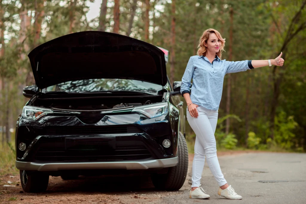 Woman hitchhiking beside a black SUV with its hood open on a forest roadside